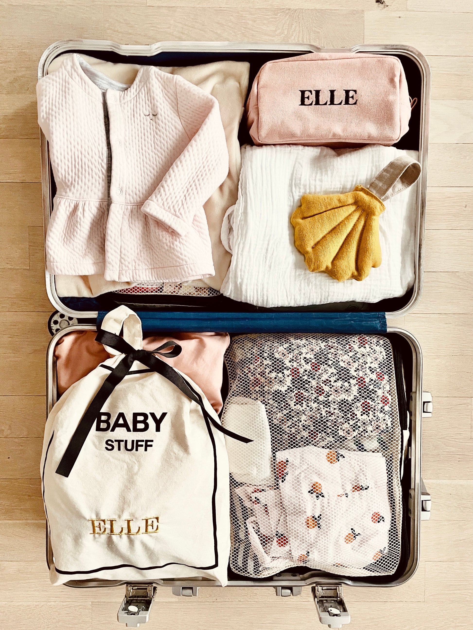 Bag-all neatly packed baby suitcase featuring personalized ELLE toiletry bag, baby clothes, and drawstring storage bag with soft pink and neutral colored essentials