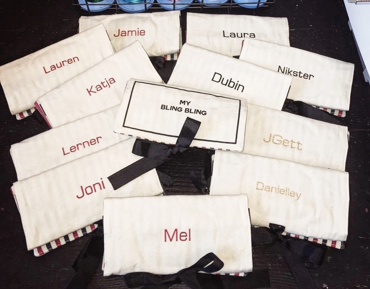 Bag-all Jewelry Organizer Travel Pouch in cream with personalized monogram names, featuring striped trim and black bow detail, arranged in a display of multiple customized pouches