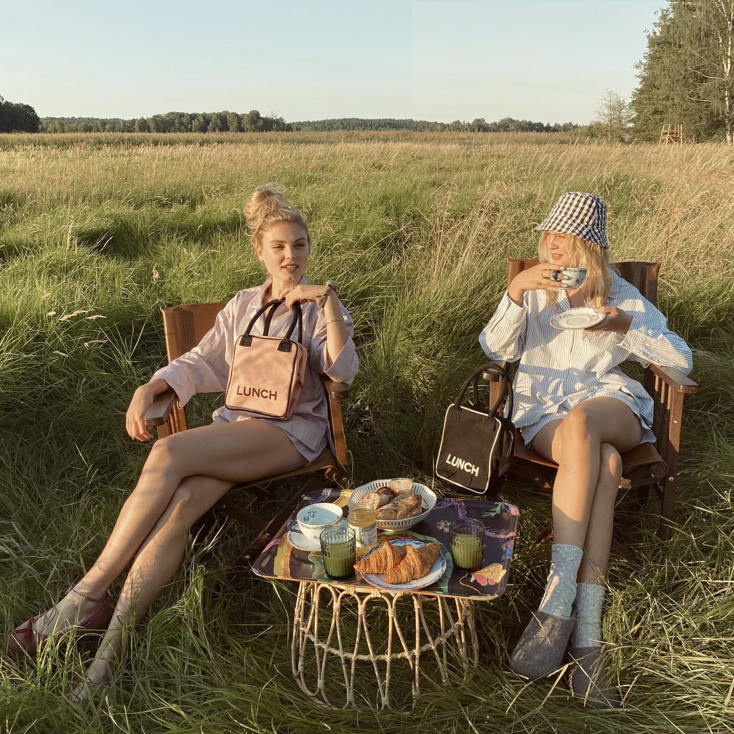 Bag-all pink insulated lunch box shown in outdoor picnic setting with vintage rattan table, featuring stylish design and practical storage for meals and snacks