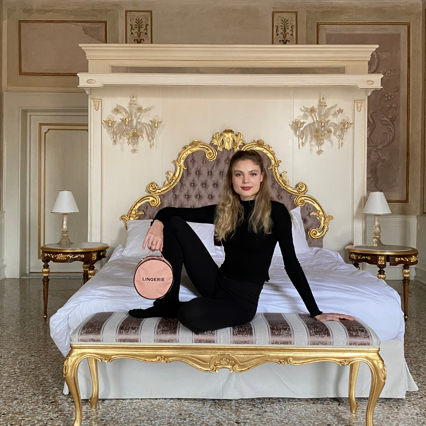 Bag-all Round Lingerie Case in blush pink shown on elegant vintage-style bed, featuring luxury cotton design with metal zipper, perfect for travel organization