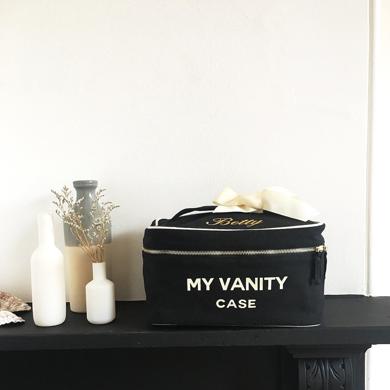 Bag-all My Vanity Large Beauty Box in black with waterproof striped lining, displayed on dark shelf with decorative white bottles and dried flowers