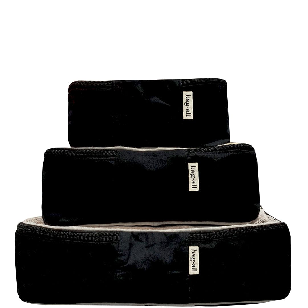 Bag-all Cotton Packing Cubes in black, 3-piece set with mesh tops and white print labels. Three stackable sizes featuring durable zippers and space-saving design for organized travel and storage.