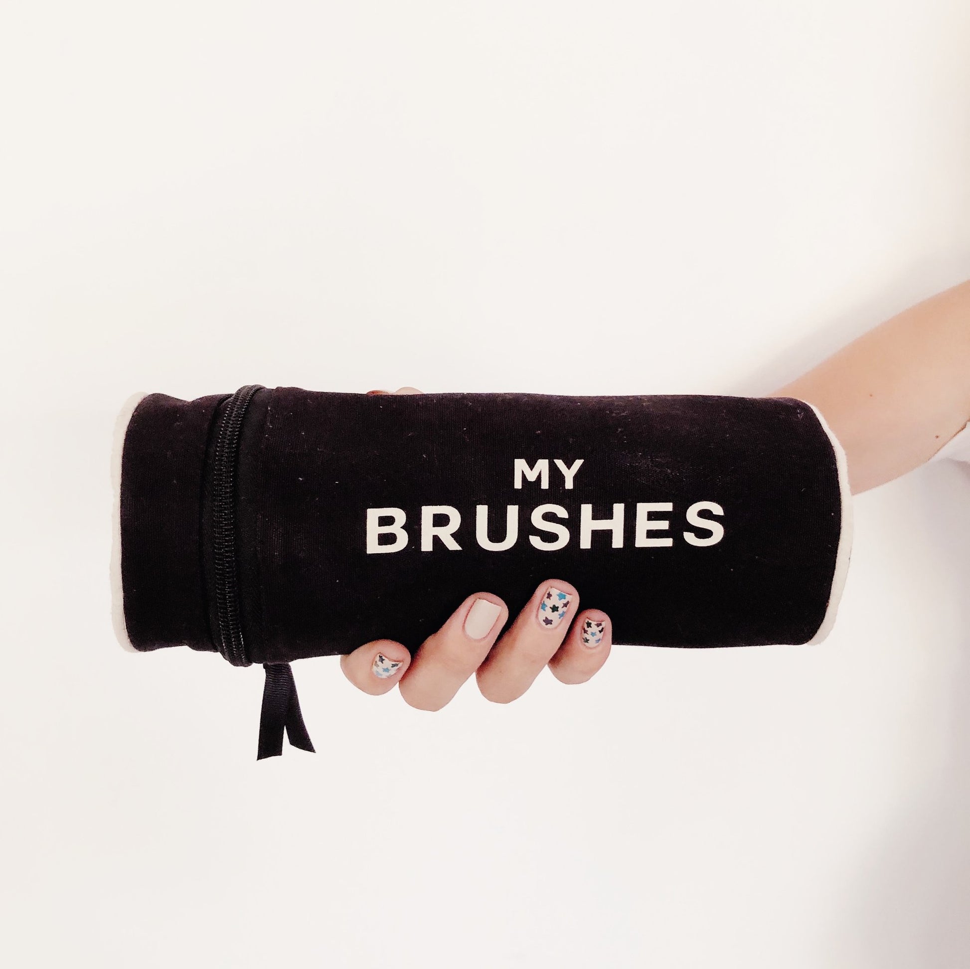 Bag-all My Brushes black velvet makeup brush organizer case with white text, held by manicured hand against white background