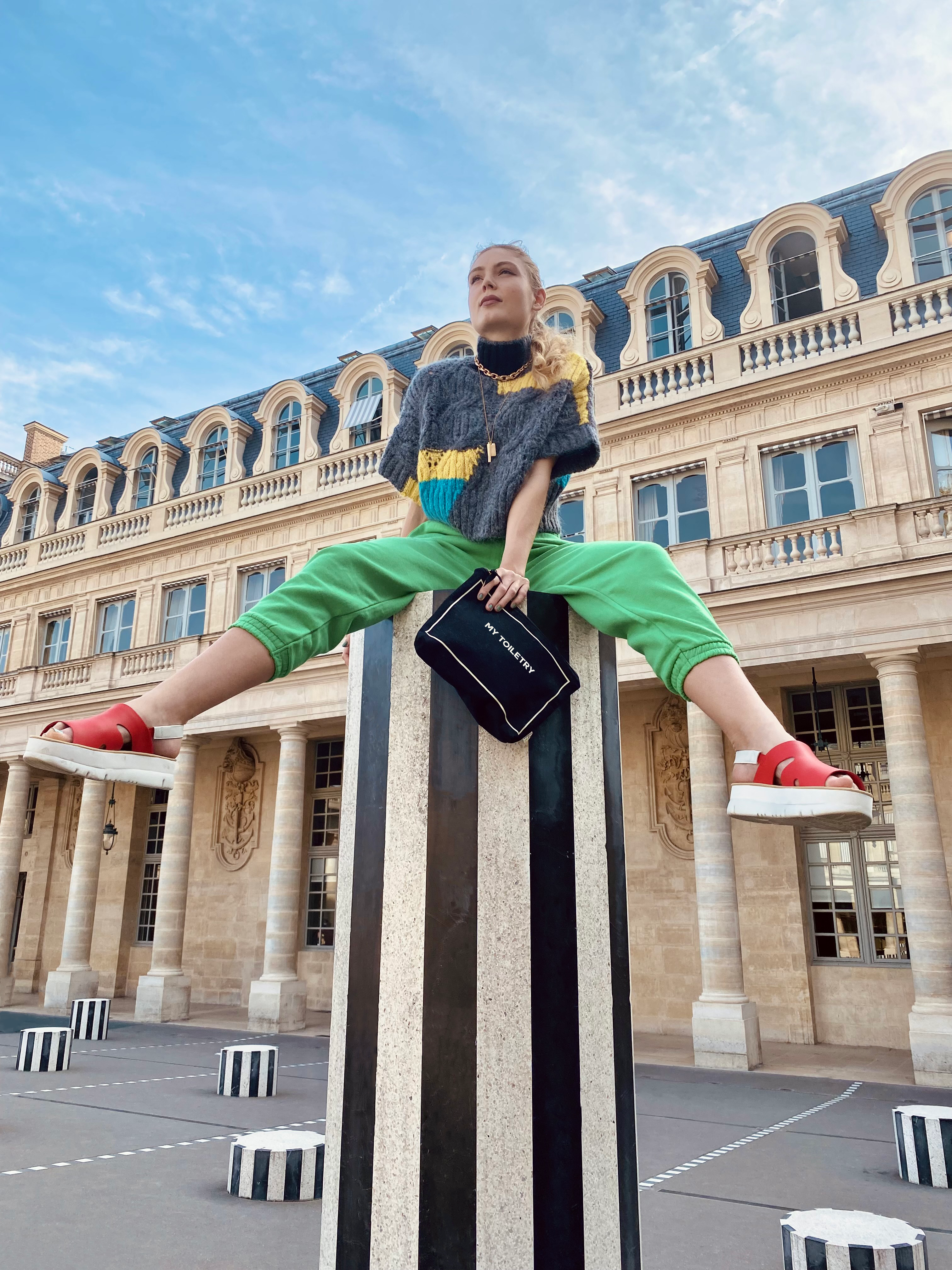 Bag-all Black Toiletry Pouch with Coated Lining shown outdoors against historic Parisian architecture at Palais Royal, featuring striped Buren columns and classic mansard roofline