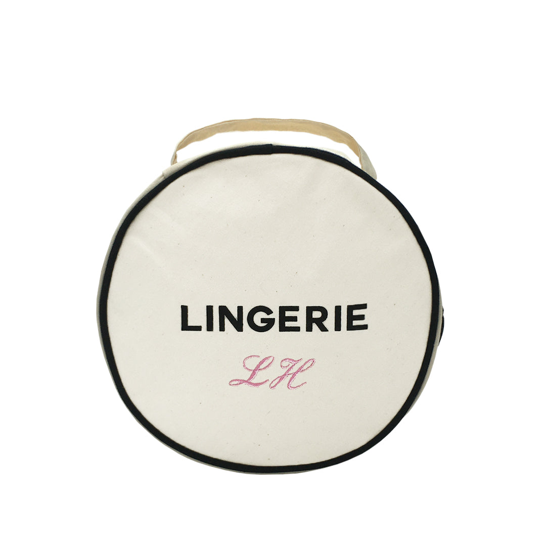 Bag-all Round Lingerie Case in cream cotton with black trim, featuring 'LINGERIE' text and monogram option, perfect for organized travel storage