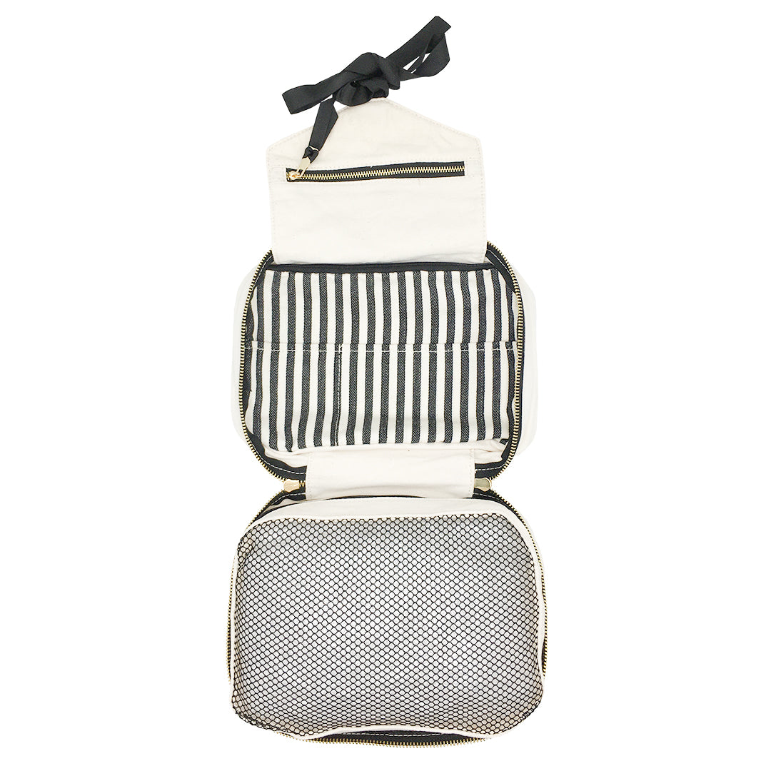 Bag-all Folding/Hanging Toiletry Case in cream with three compartments, striped interior, mesh pocket, and hanging ribbon. Travel-ready organizer with convenient zipper closure and grab handle.
