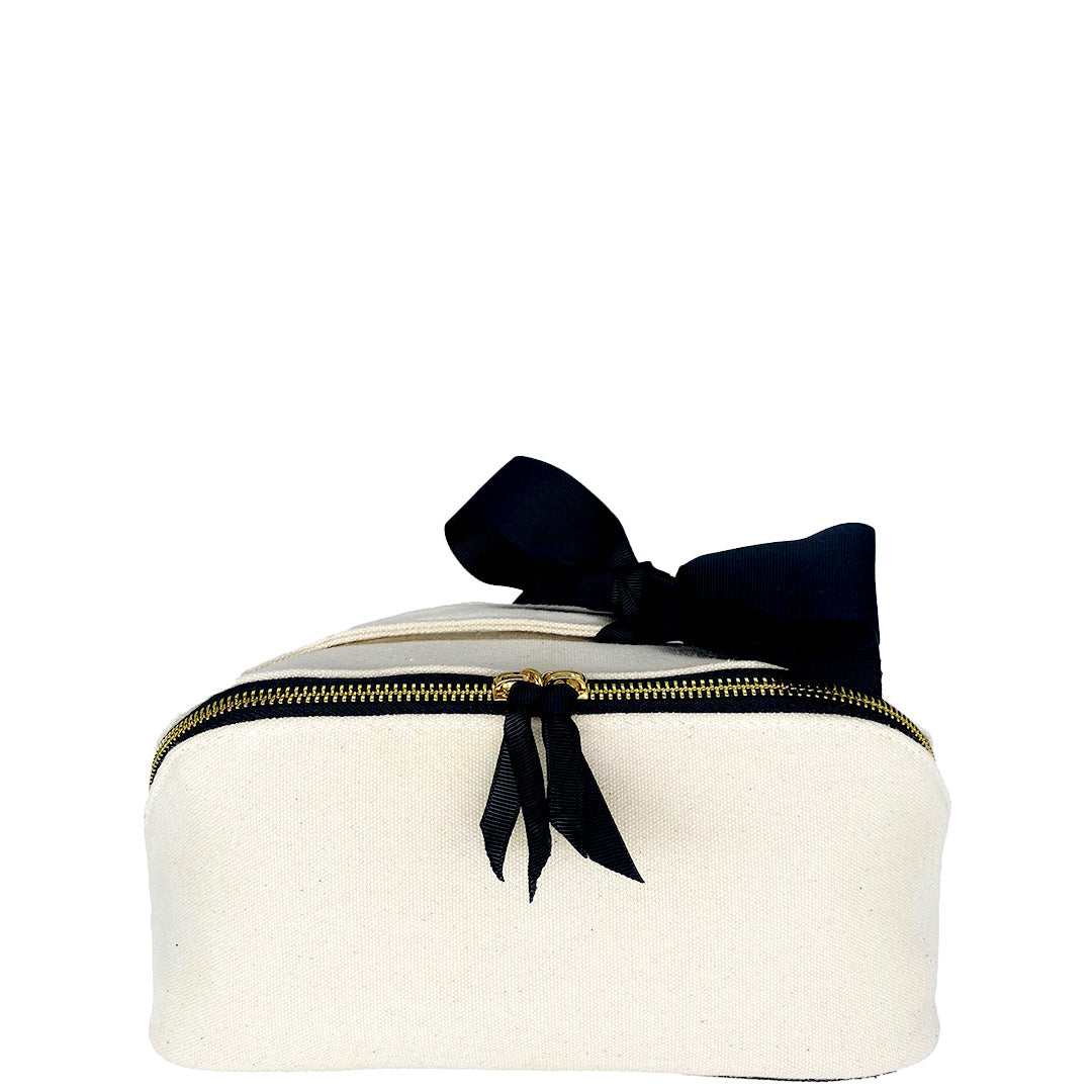 Bag-all's elegant cream cotton cosmetic case featuring black bow detail and gold zipper, perfect for organizing beauty essentials in style