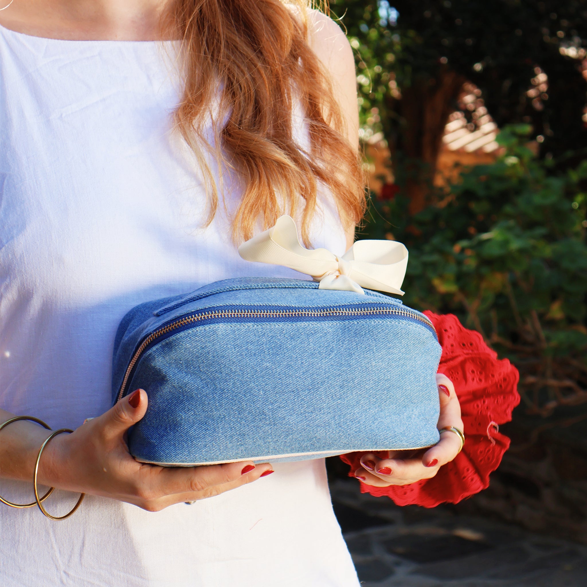 Woman holding Bag-all expandable denim makeup organizer with zipper and bow detail outdoors