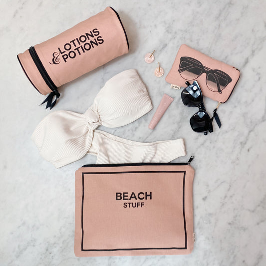 Bag-all Stylish Beach Essential Set in pink/blush featuring waterproof pouch, sunglasses case and lotions bag, displayed with white swimwear and beach accessories on marble surface