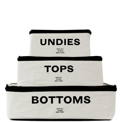 Bag-all Cotton Packing Cubes in cream with black trim, labeled Undies, Tops, and Bottoms. Three-piece set in graduating sizes with mesh panels for organization and visibility.