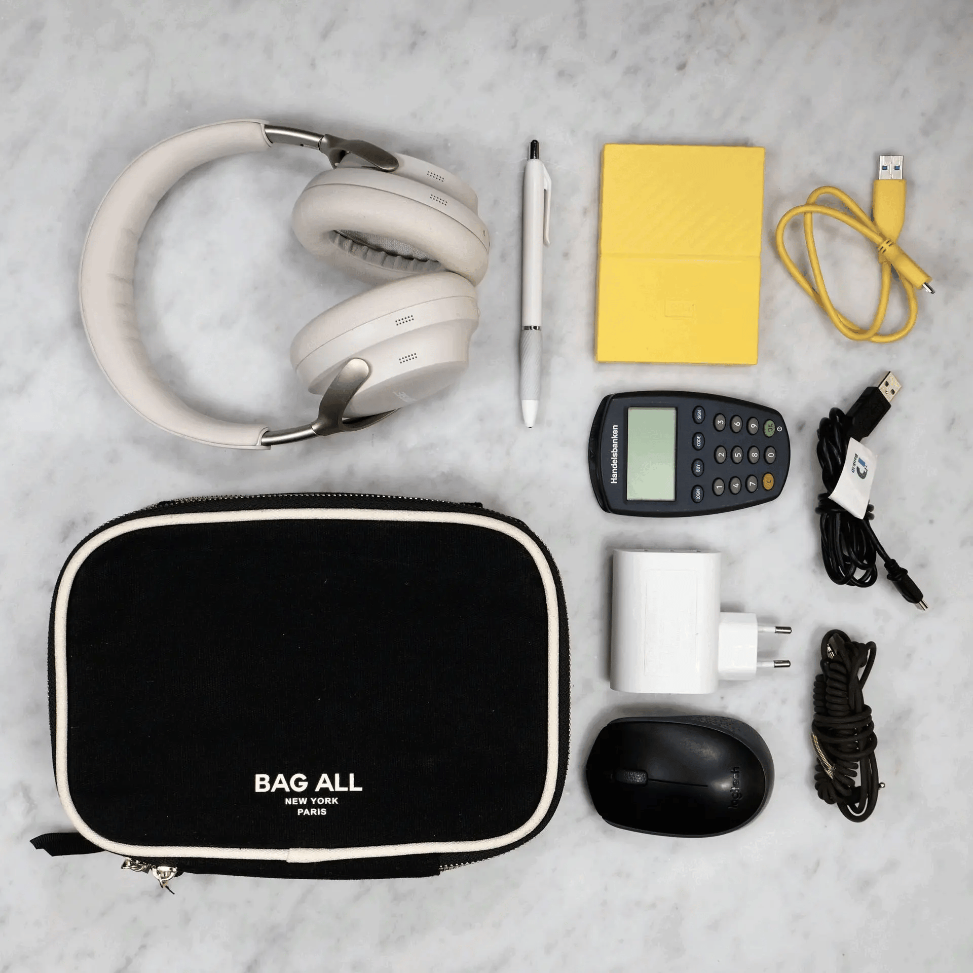Black double-sided tech case by Bag-all with headphones, charger, mouse, pen, and cables on marble surface