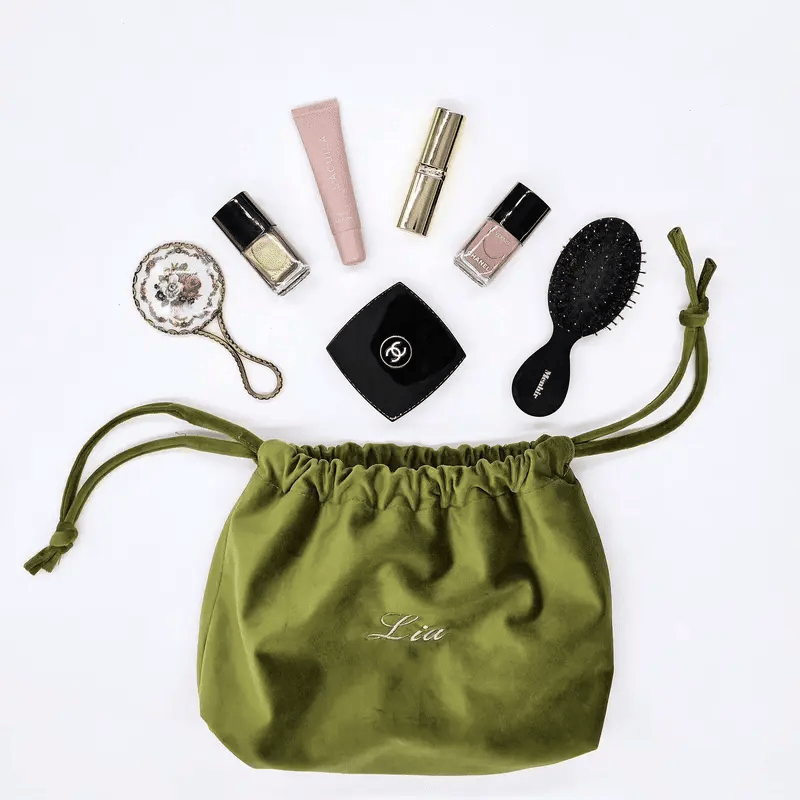 Bag-all green eco velvet drawstring makeup bag personalized with name surrounded by beauty essentials on white background