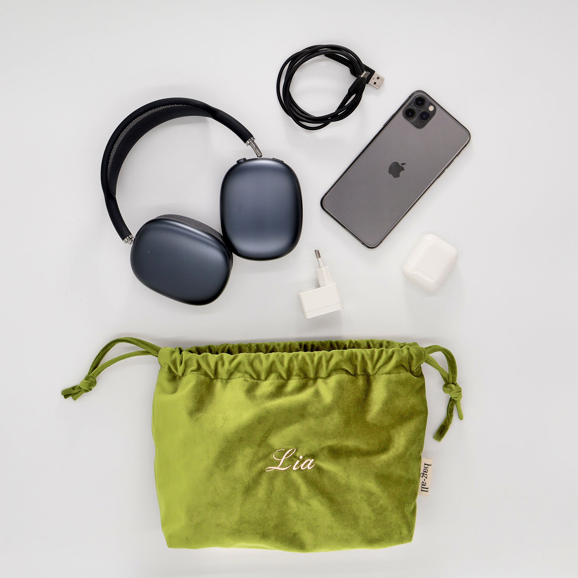 Green eco velvet drawstring tech pouch by Bag-all with earbuds, charger, cables, and wireless headphones neatly arranged nearby
