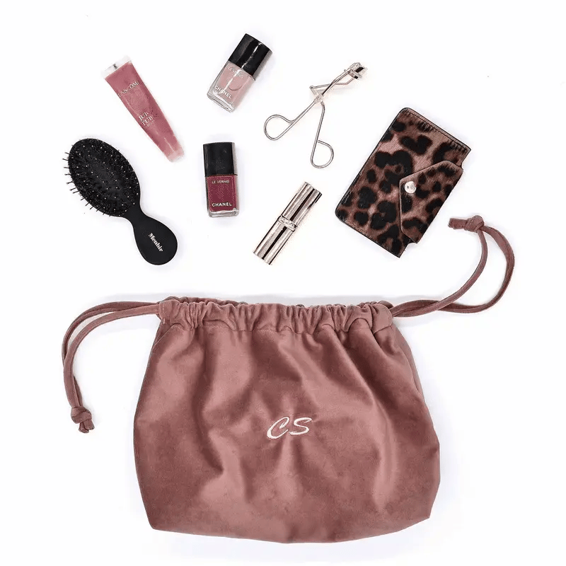 Pink velvet drawstring makeup bag by Bag-all with beauty essentials, brush, and travel accessories neatly arranged nearby