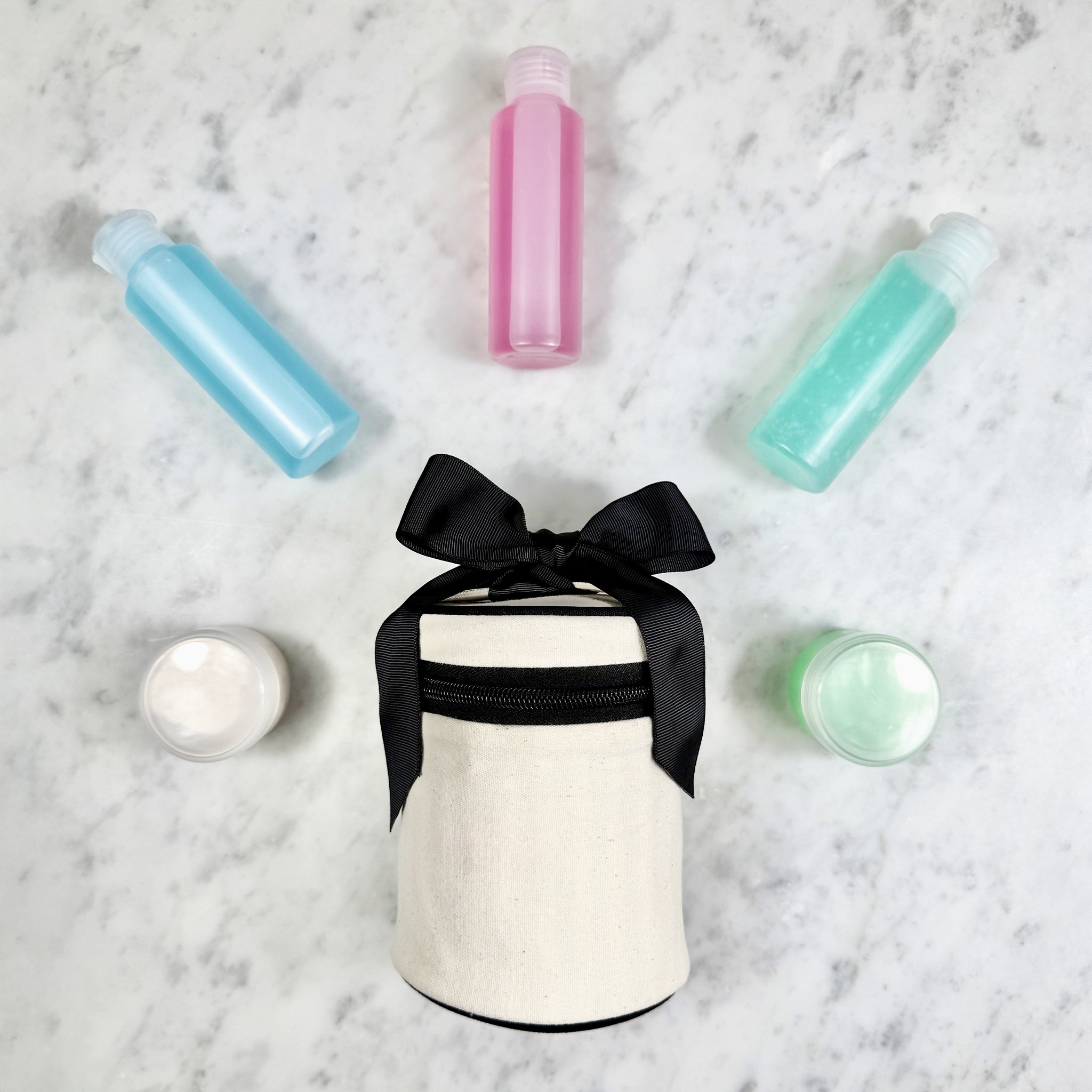 Bag-all cream carry on essentials set with three travel bottles and two small cream containers on marble surface