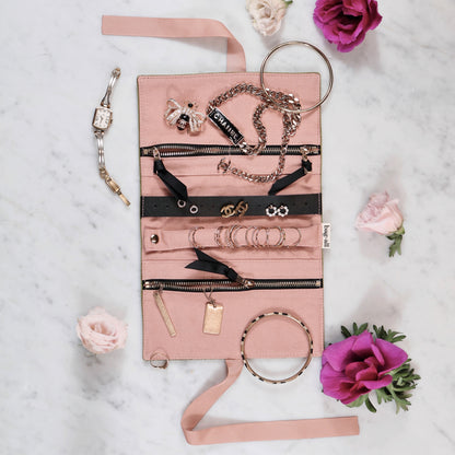 Bag-all Couture Jewelry Roll in pink features multiple compartments and storage solutions for rings, necklaces, and earrings, displayed open with elegant jewelry pieces on marble surface with pink and purple roses