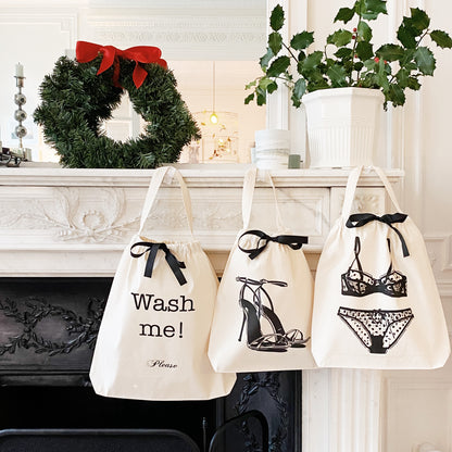 Three cream Bag-all bags with black bows and laundry-themed prints hanging on white fireplace mantel with Christmas wreath