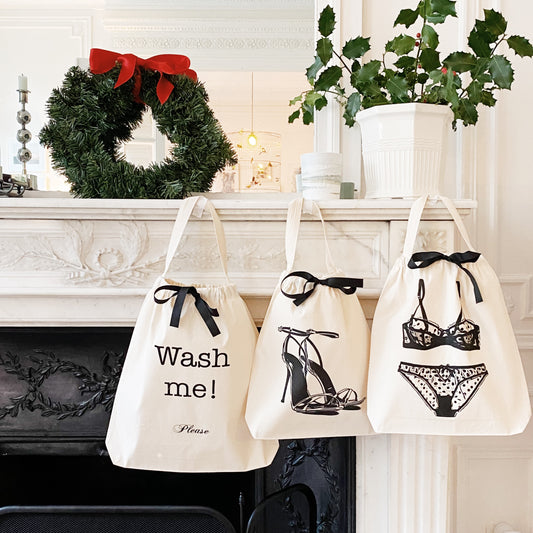Three cream Bag-all bags with black bows and laundry-themed prints hanging on white fireplace mantel with Christmas wreath