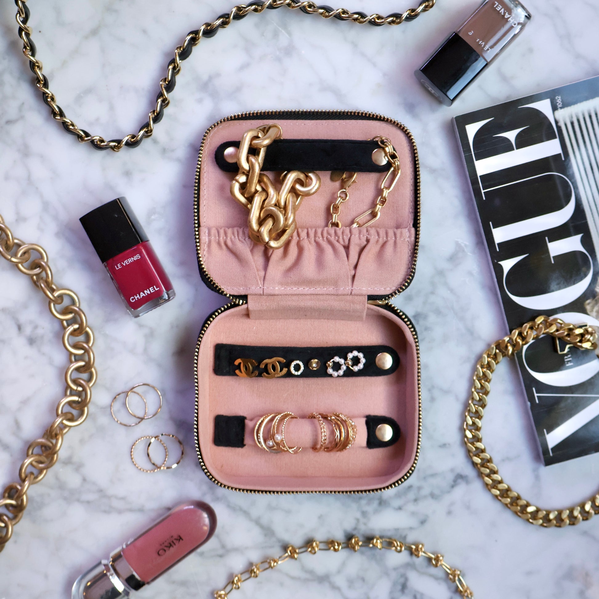 Open black Bag-all eco velvet jewelry organizer case with gold chain, earrings, rings, and makeup on marble table