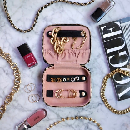 Open black Bag-all eco velvet jewelry organizer case with gold chain, earrings, rings, and makeup on marble table