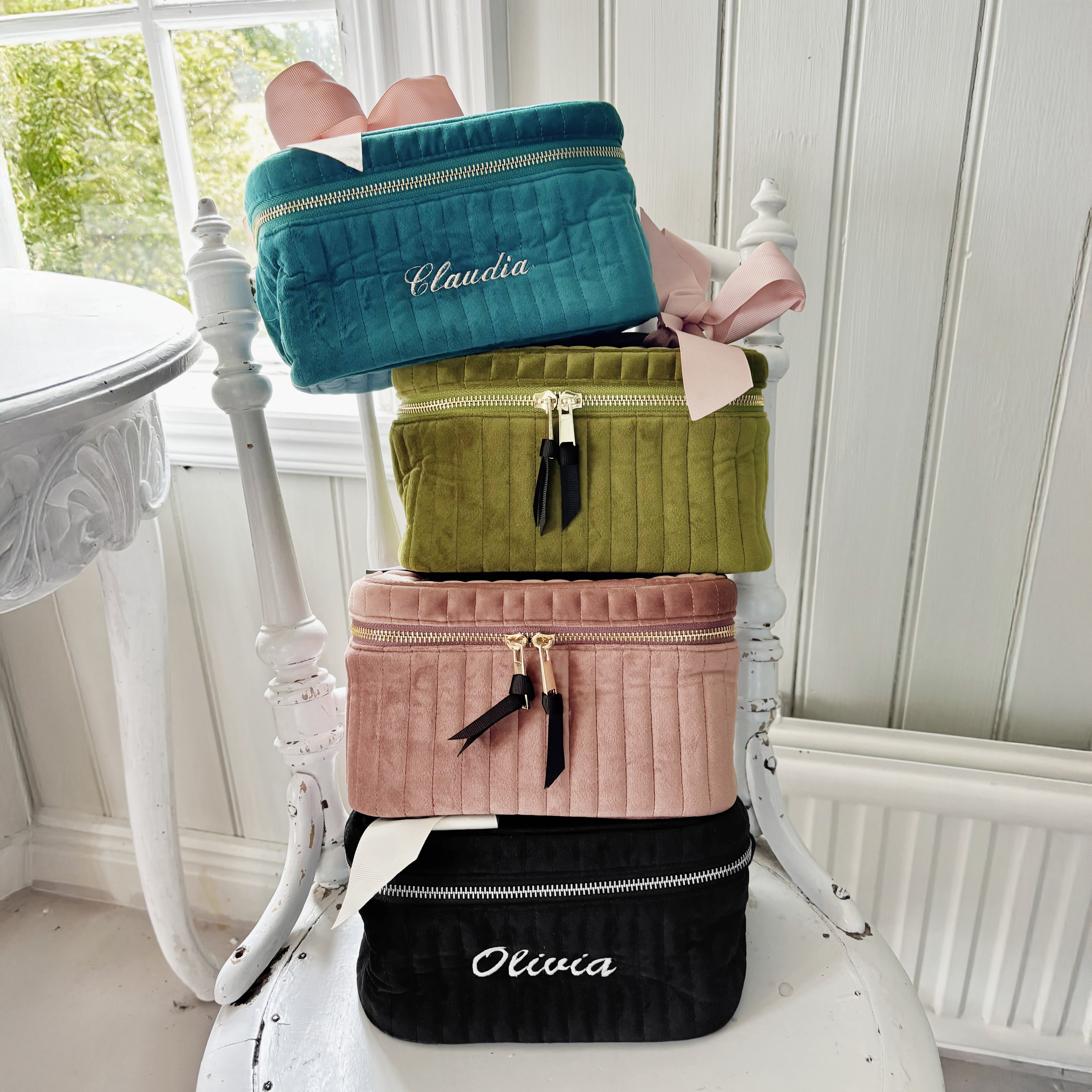 Stack of quilted eco velvet makeup cases in various colors including black with Bag-all branding displayed on white chair