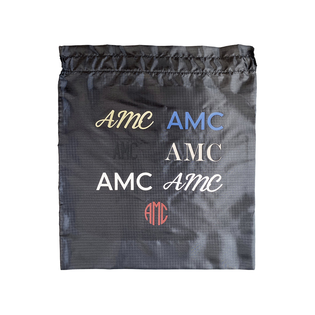 Bag-all personalized vinyl bag displaying various AMC monogram styles in different fonts and colors on black recycled nylon, showcasing custom vinyl personalization options