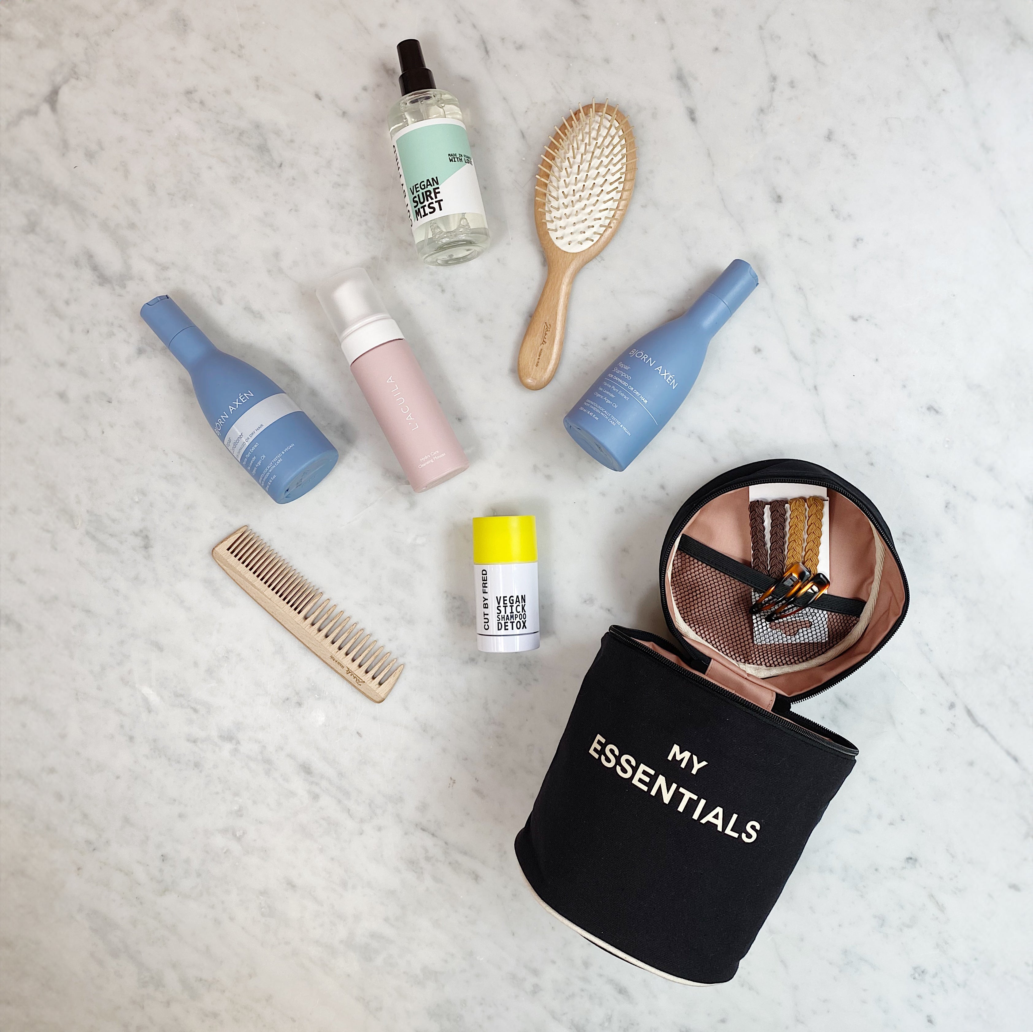 Bag-all Round My Essentials Case in black with beauty products, hairbrush, and toiletries organized neatly on marble surface showcasing spacious storage and waterproof lining