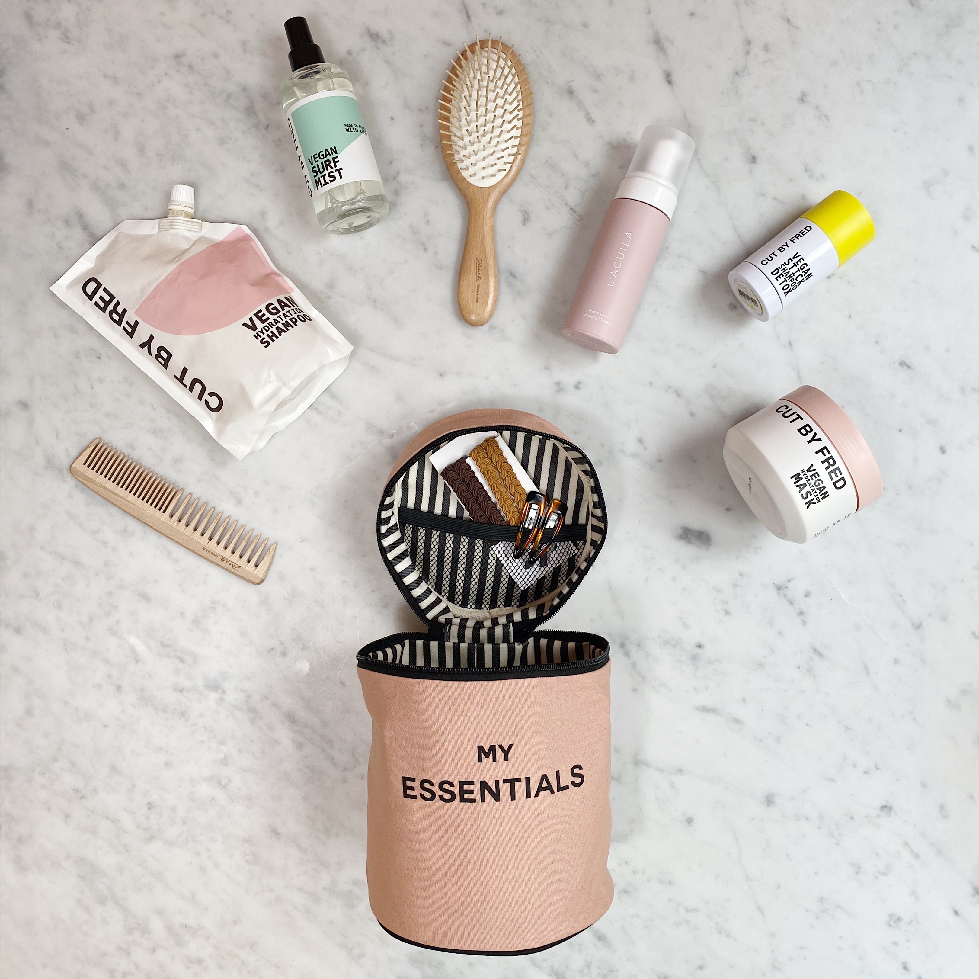Bag-all Round My Essentials Case in pink with coated interior, shown open displaying beauty products, brushes and toiletries on marble surface, demonstrating storage capacity and organization