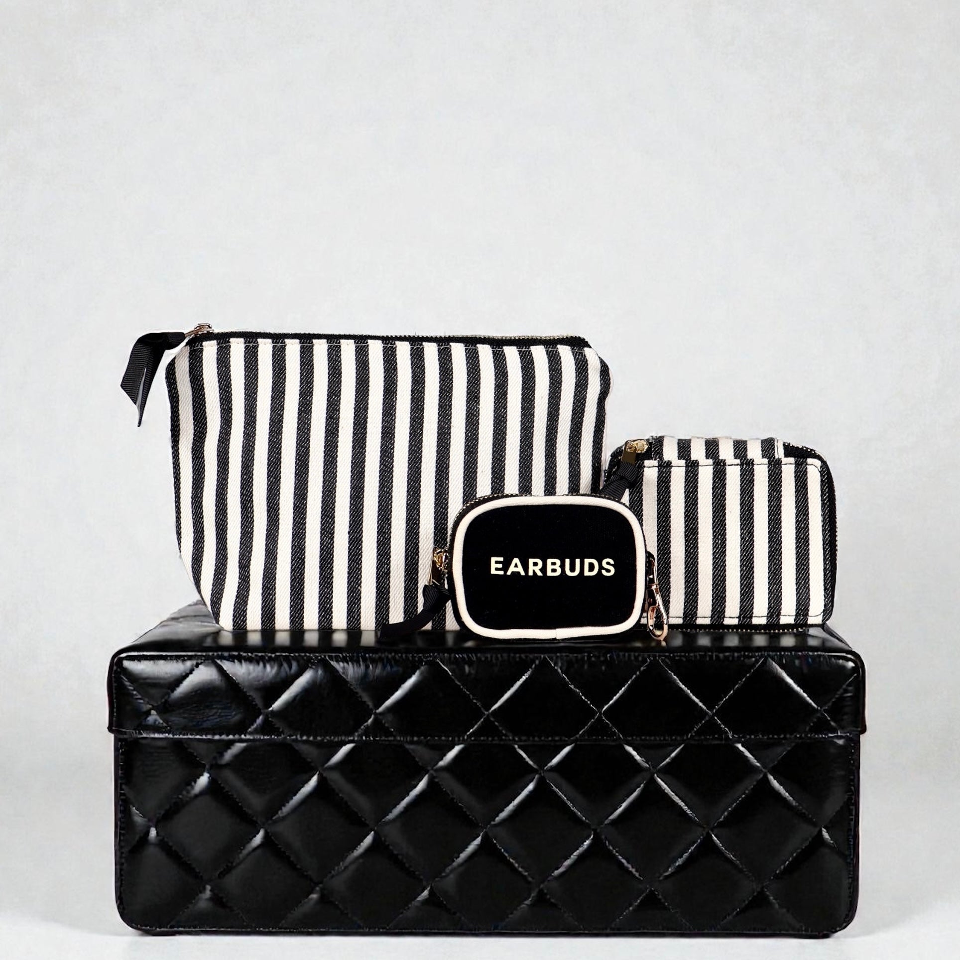 Set of Bag-all striped handbag organizers featuring trinket, makeup, and earbuds cases on black quilted box background