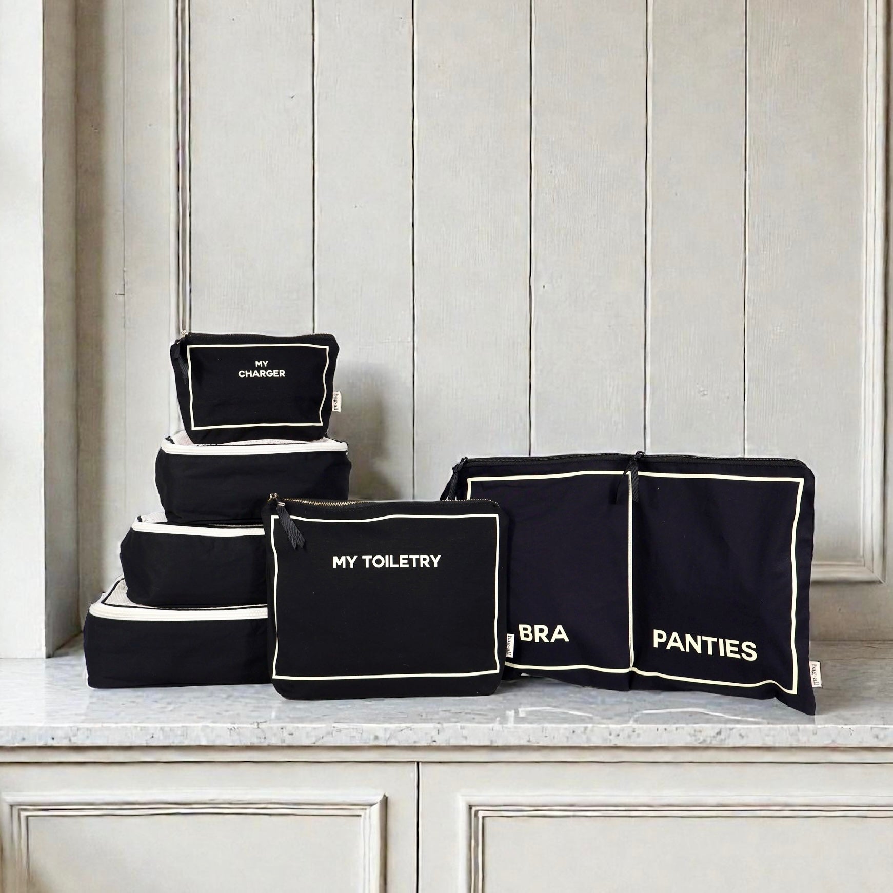 Set of black Bag-all packing cubes and pouches labeled My Toiletry, Bra, Panties, and My Charger on marble surface