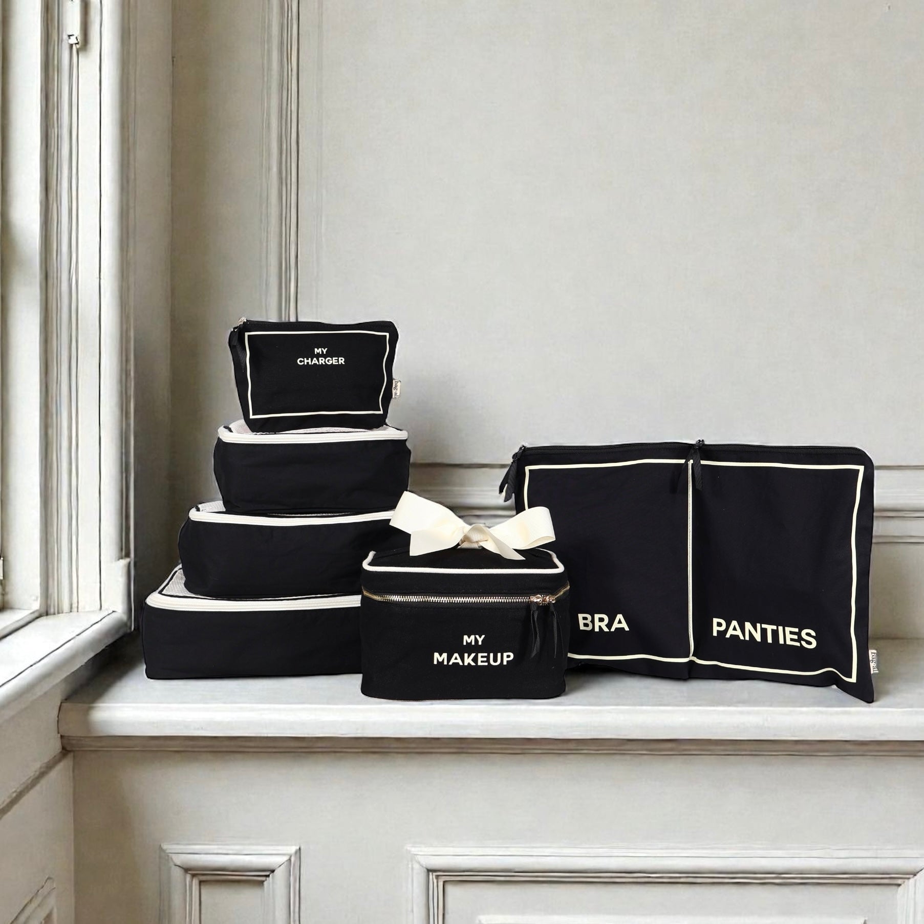Set of black Bag-all cotton travel organizers with white trim labeled charger makeup bra and panties