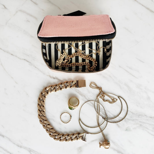 Bag-all Pink Jewelry Trinket Box with striped lining and gold zipper, displayed with gold jewelry pieces including chain bracelet, rings and necklaces on marble surface