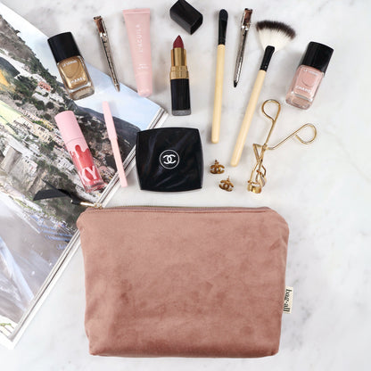 Pink eco velvet makeup and jewelry pouch from Bag-all with brushes, lipsticks, nail polish, and accessories on marble surface