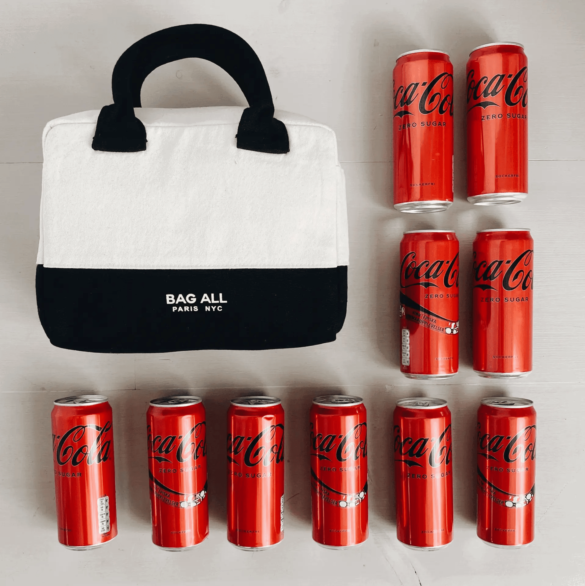 Bag-all Stylish Monogram Lunch Box in cream and black with contrast handles shown with Coca-Cola cans for size reference, demonstrating spacious insulated storage capacity