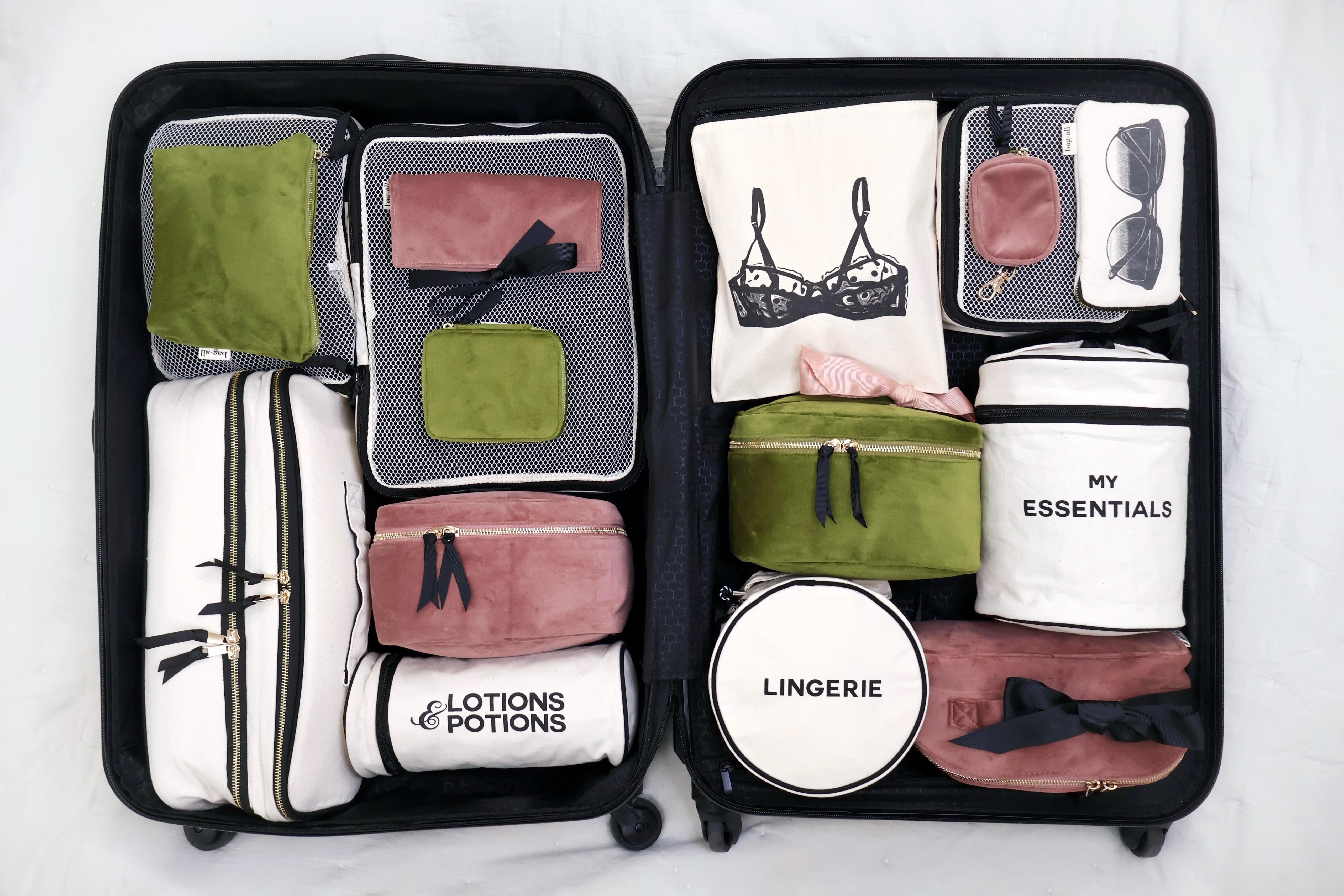 Open suitcase neatly arranged with personalized cotton bags and packing cubes in soft pink, white, and olive green for travel organization by Bag-all