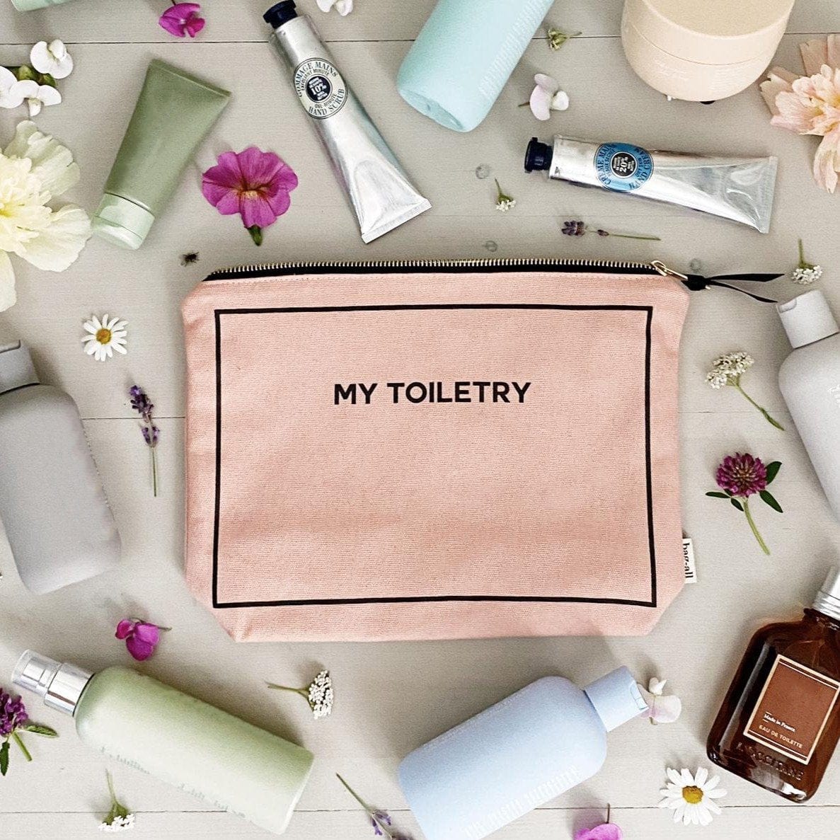 Bag-all Toiletry Travel Gift Set Deal 4-Pack in Pink featuring cotton toiletry pouch with "My Toiletry" text, surrounded by beauty products and flowers on light wooden surface