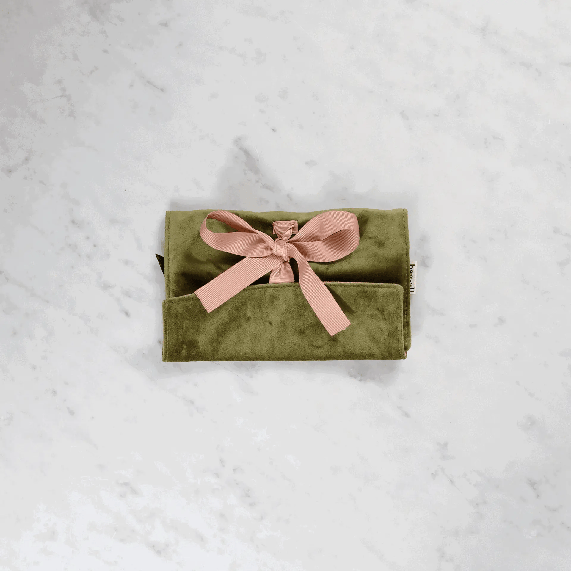 Bag-all Couture Jewelry Roll in green velvet with pink bow, featuring multiple compartments for organizing jewelry, displayed on marble surface