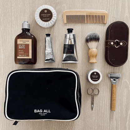 Bag-all Double Sided Toiletry Case in Black shown with grooming essentials: shaving cream, wooden comb, after-shave balm, shaving brush, and manicure tools. Waterproof cotton case with dual zippers and white trim.