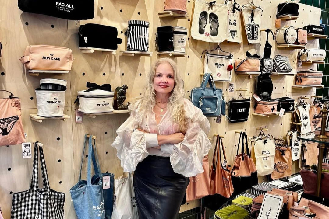 Woman standing in a store with various handbags displayed on the wall behind her.