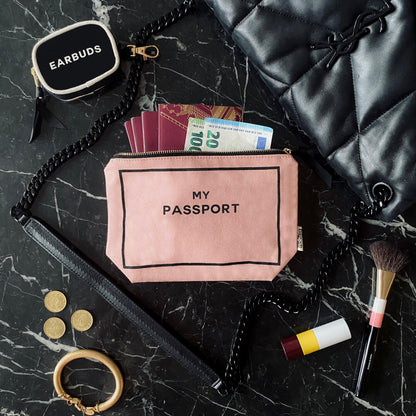 Bag-all pink passport organizer with cash and documents on marble surface with makeup and accessories nearby