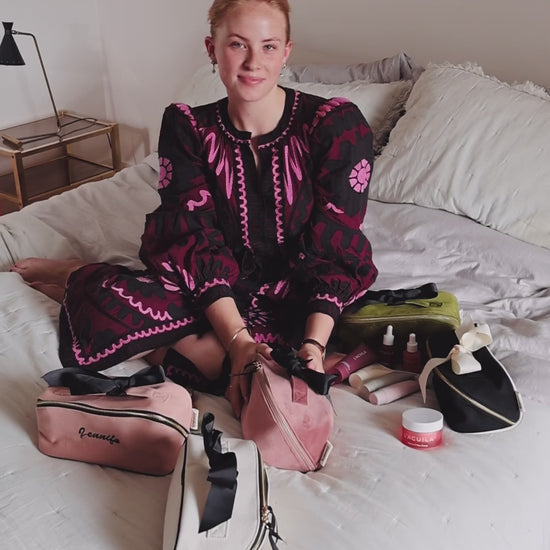 Woman sitting on a bed with Bag-all makeup and toiletry organizers, including the Accordion Box in Pink Velvet. Stylish and practical beauty storage