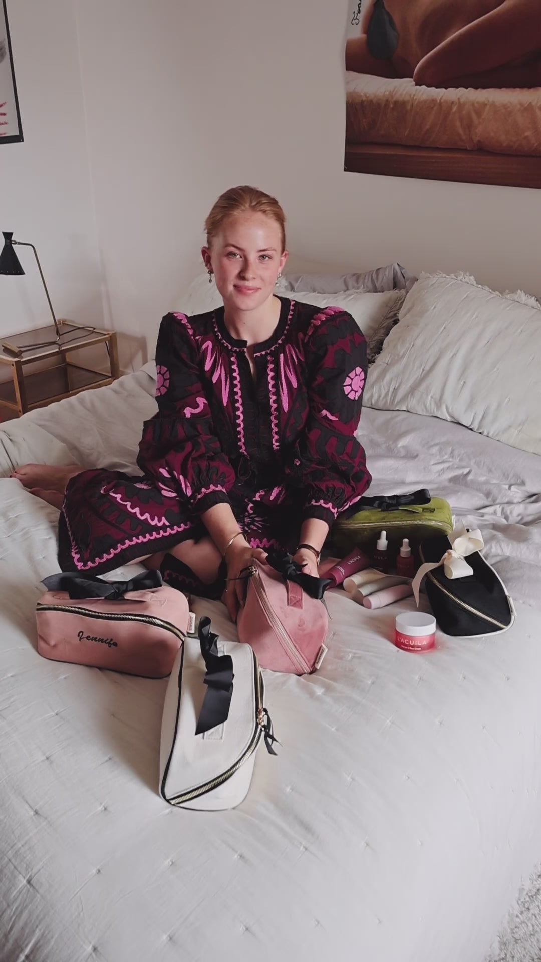 Woman sitting on a bed with Bag-all makeup and toiletry organizers, including the Accordion Box in Pink Velvet. Stylish and practical beauty storage