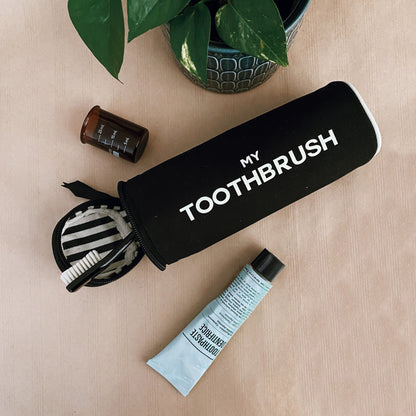 Bag-all black travel toothbrush organizer pouch with white text MY TOOTHBRUSH on beige surface with toiletries nearby