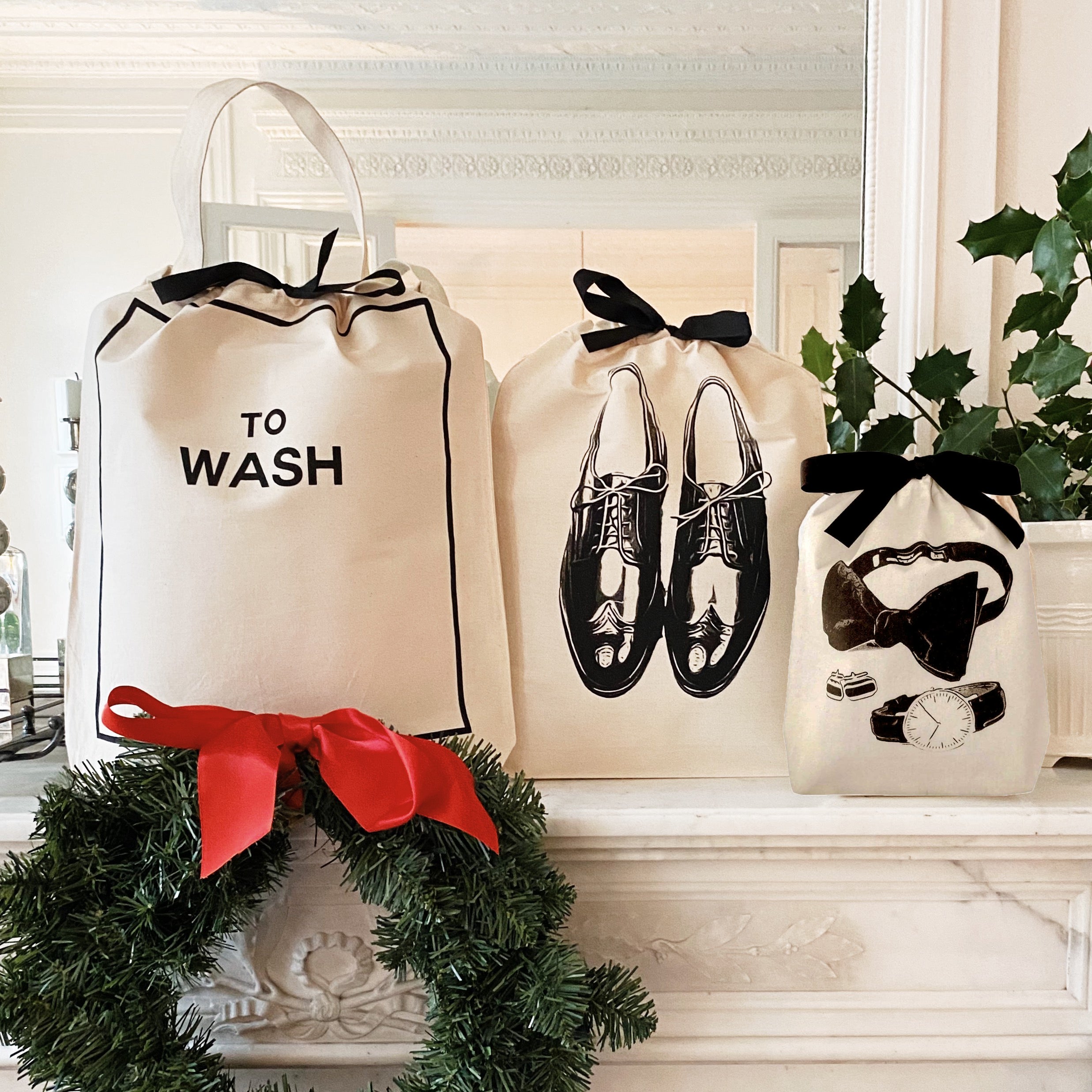 Three cream Bag-all storage bags with black prints and bows displayed on mantel with holiday wreath and greenery