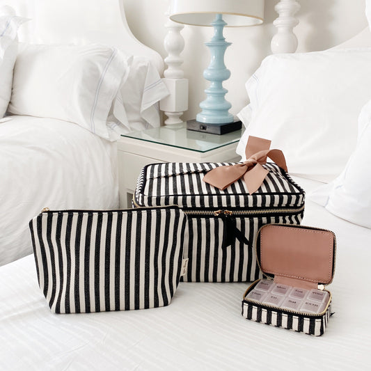 Bag-all Cutest Striped Travel Gift Set 3-Pack featuring black and white striped cotton makeup bag, toiletry case, and pill organizer with pink bow accent on white bedding