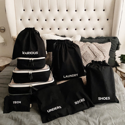 Bag-all travel organizer set featuring black cotton bags with white text labels - Various, Laundry, Tech, Unders, Socks, and Shoes - perfect for keeping belongings sorted