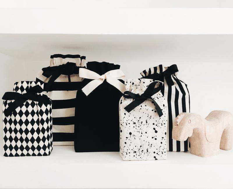 Bag-all Gift Bag Black Medium shown with collection of stylish reusable fabric gift bags featuring black and white patterns, stripes, and splatter designs, all adorned with elegant ribbon closures