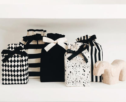 Bag-all Gift Bag Black Medium shown with collection of stylish reusable fabric gift bags featuring black and white patterns, stripes, and splatter designs, all adorned with elegant ribbon closures