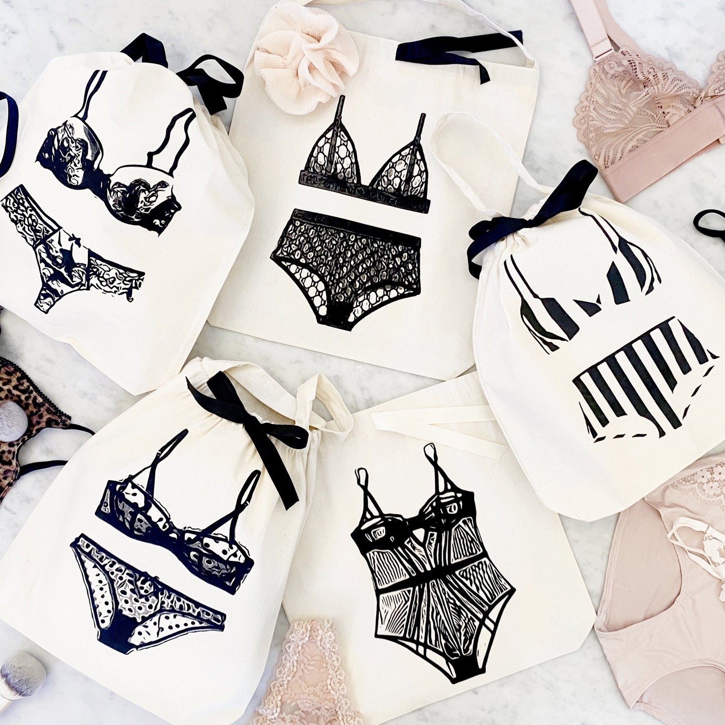 Bag-all lingerie organizing bags featuring stylish black and white illustrations of various lingerie sets on cotton bags with black ribbon ties, perfect for travel and storage
