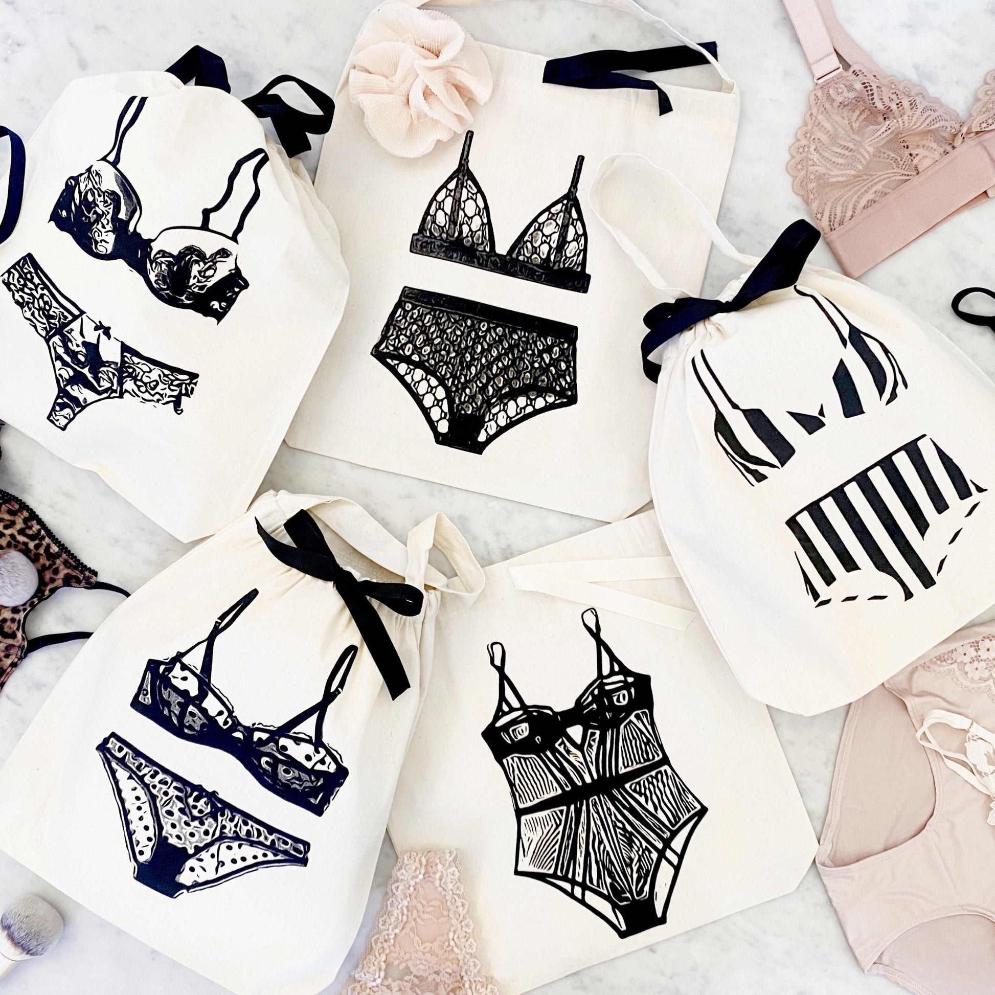 Bag-all lingerie organizing bags featuring stylish black and white illustrations of various lingerie sets on cotton bags with black ribbon ties, perfect for travel and storage